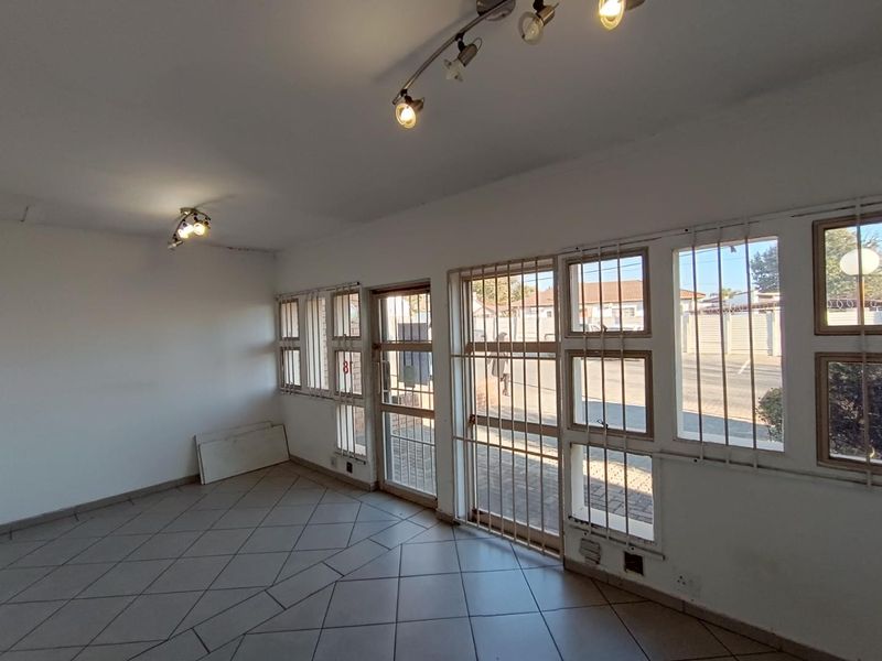 An empty commercial space featuring ceramic tiled flooring, track lighting, and large windows with security bars, offering a blank canvas for business customization.