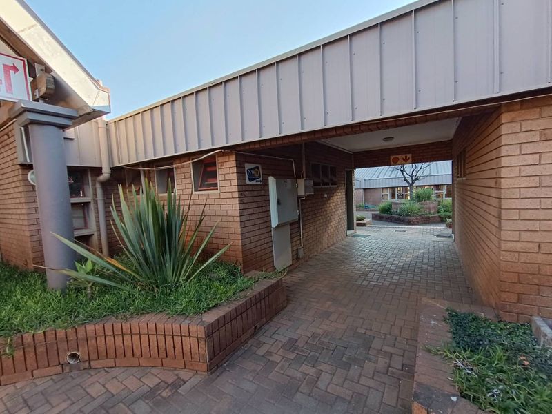 A covered brick-paved walkway connecting commercial building sections, featuring face brick construction and integrated raised garden planters.