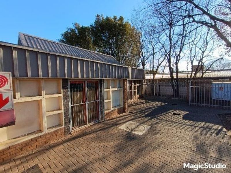 Front exterior view of a commercial building featuring brick paving, metal roofing, and secure metal gate access.