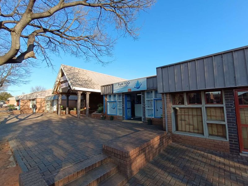Front exterior view of a commercial retail complex featuring brick paving, metal roofing, and multiple storefront entrances.