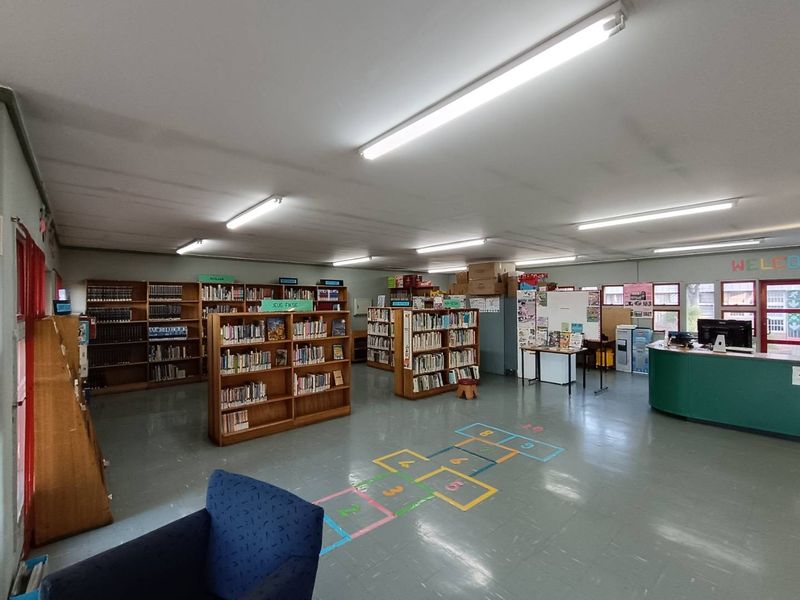 A spacious commercial library or educational facility featuring vinyl flooring, built-in shelving units, and a reception desk with overhead fluorescent lighting.