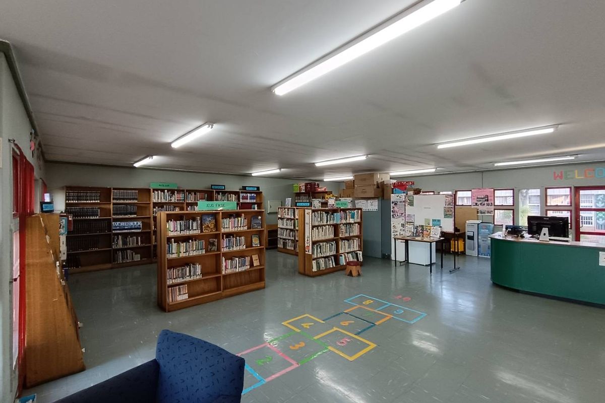 A spacious commercial library or educational facility featuring vinyl flooring, built-in shelving units, and a reception desk with overhead fluorescent lighting.