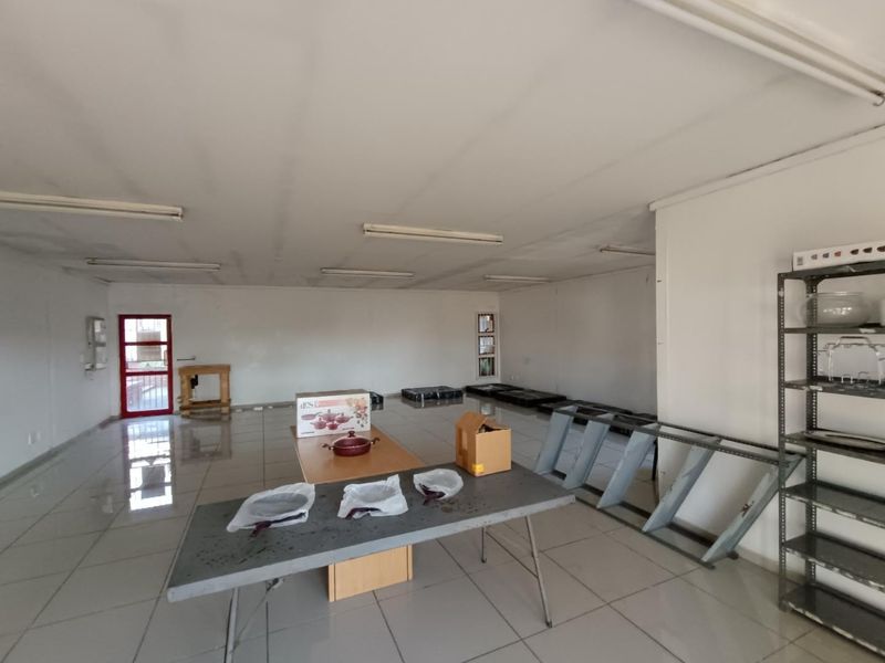 An open-plan commercial space featuring tiled flooring, fluorescent lighting, and a red-framed glass entrance door, suitable for retail or office use.