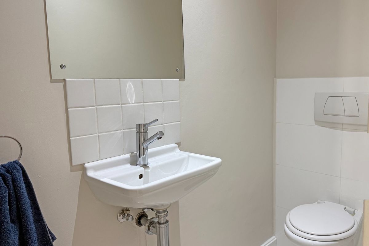 A clean and modern guest bathroom featuring a wall-mounted basin with chrome fixtures and a wall-hung toilet with a concealed cistern.