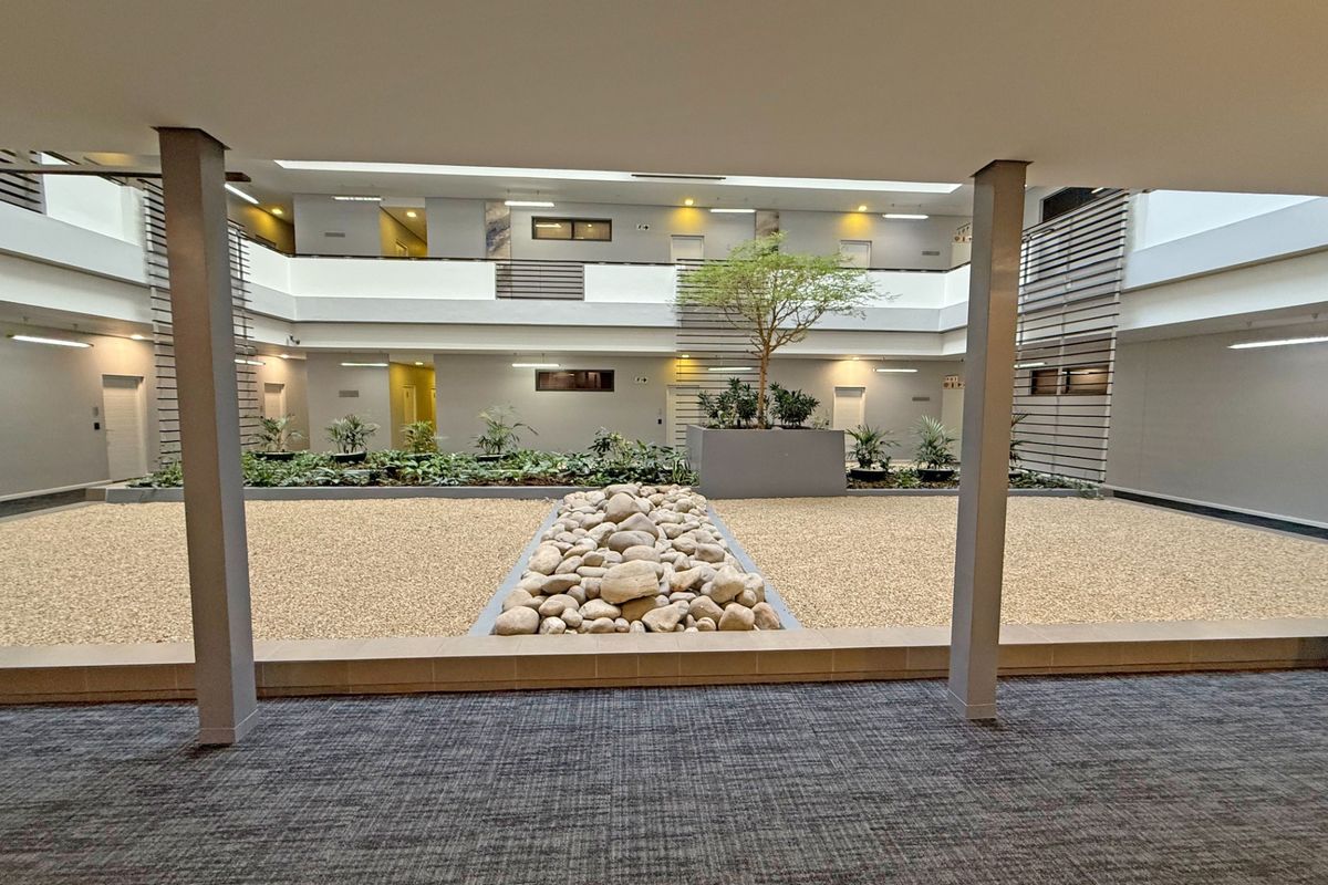A well-maintained central courtyard featuring a landscaped garden, stone pathway, and gravel ground cover, surrounded by multi-level apartment building corridors.