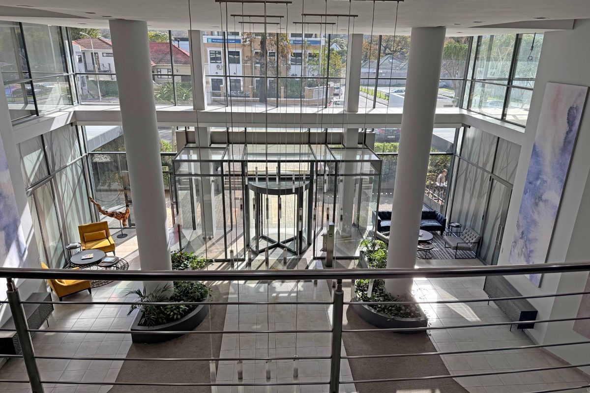 A spacious, modern apartment building lobby featuring a revolving entrance door, floor-to-ceiling glass windows, and a double-volume ceiling with contemporary pendant lighting.