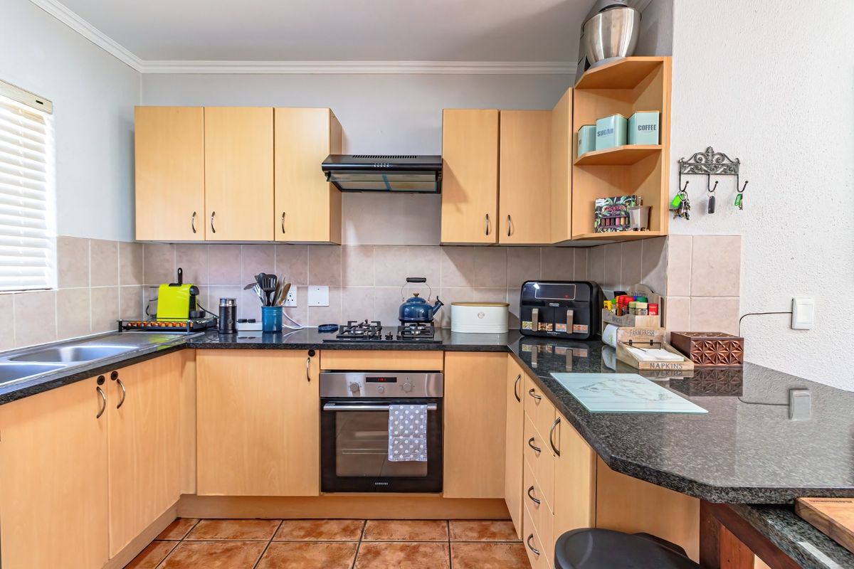 Functional kitchen featuring light wood cabinetry, granite countertops, built-in oven, gas hob, and tiled flooring, offering a practical layout for daily meal preparation.