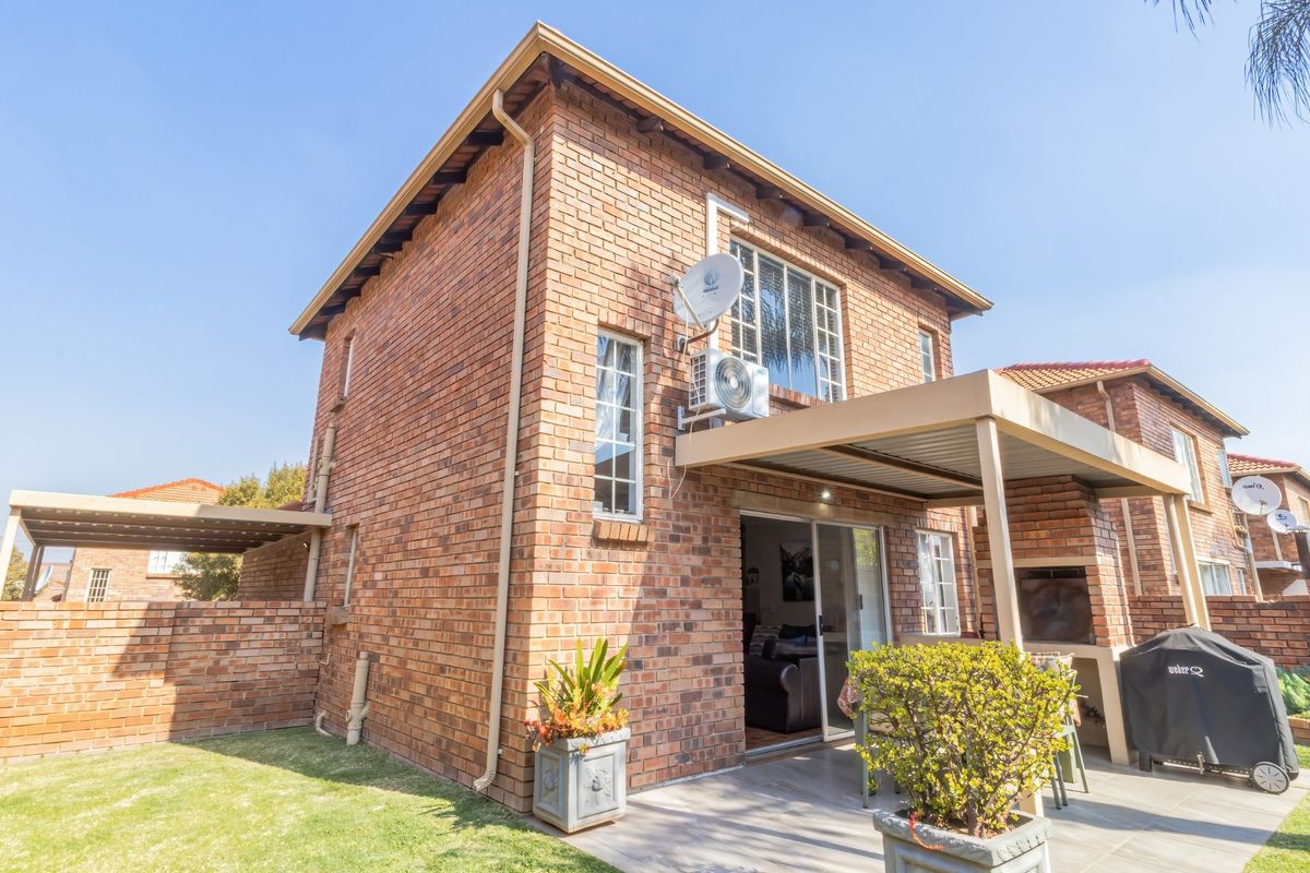 Rear view of a face brick townhouse featuring a covered patio with a built-in braai, sliding door access, and a private garden area.