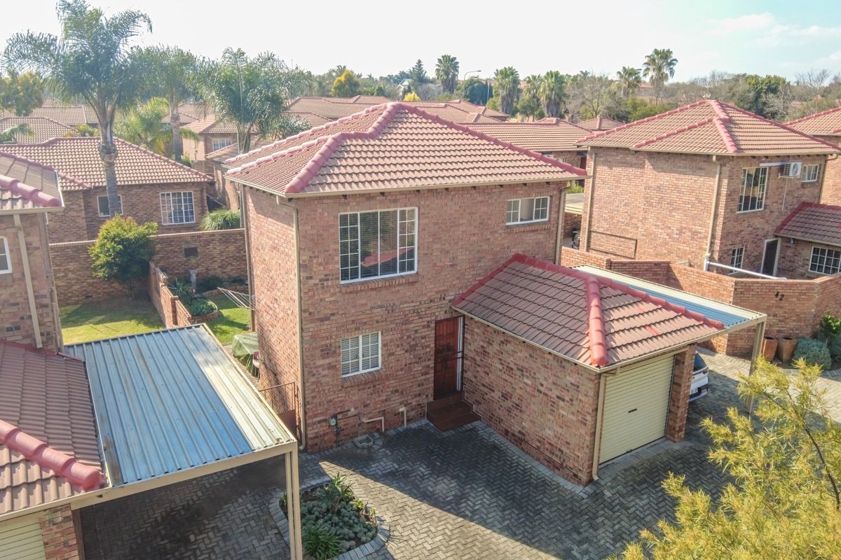 Aerial view of a double-story face brick townhouse featuring a tiled roof, attached garage, and paved driveway within a residential complex.