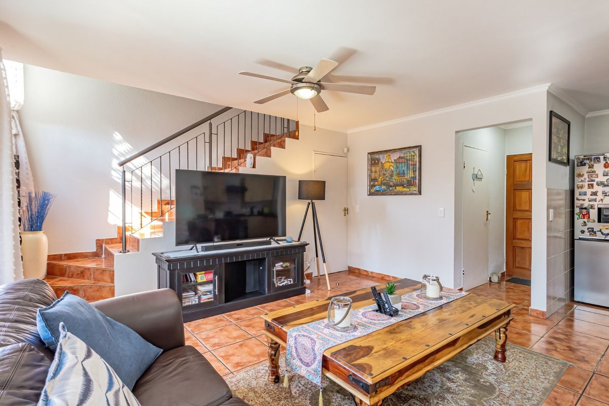 A living room featuring tiled flooring, a ceiling fan, and an open staircase with a metal railing, leading to upper levels.
