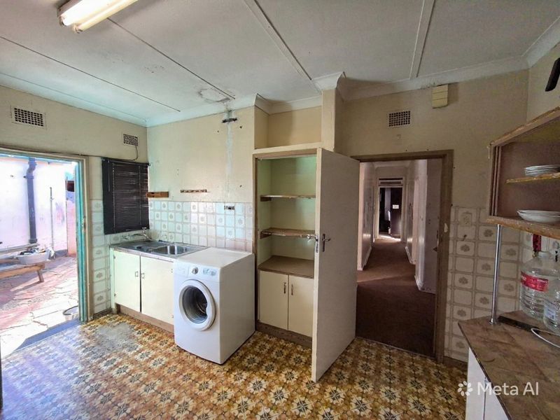A dated scullery or laundry area featuring a stainless steel sink, built-in cabinetry, and tiled splashbacks, requiring significant renovation and cosmetic updates.