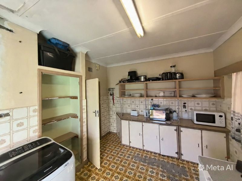 A dated scullery or utility area featuring built-in cabinetry, open shelving, and tiled splashbacks, requiring modernization and cosmetic updates.