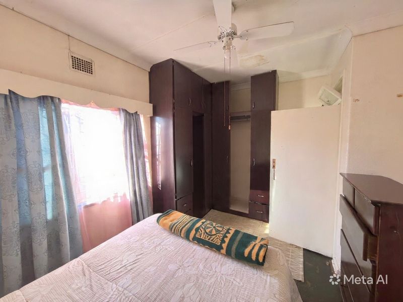Bedroom featuring built-in dark wood cupboards and a ceiling fan, showing signs of ceiling water damage and general wear.