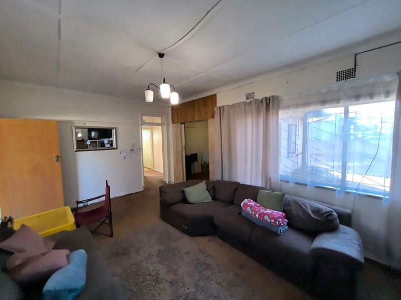 A living room featuring ceiling tiles, security bars on windows, and a sliding door, showing signs of wear and requiring cosmetic updates.