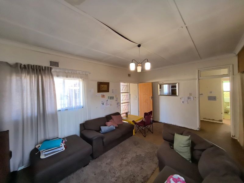 A living room area featuring standard ceiling finishes, security gate access, and neutral wall tones, requiring cosmetic updates to improve overall presentation.