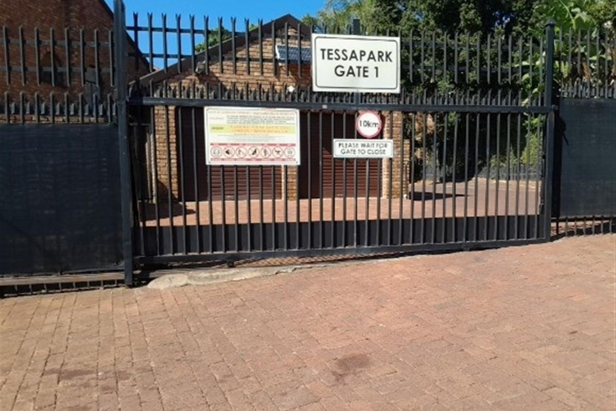 Front entrance view of the property featuring a secure metal gate, brick driveway, and garage access.