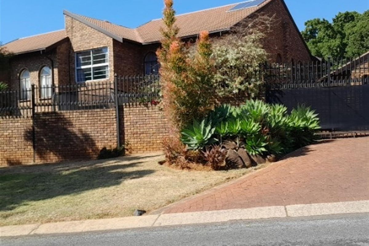 Front view of a face brick house featuring a tiled roof with solar panels, secure wrought iron fencing, and a paved driveway.