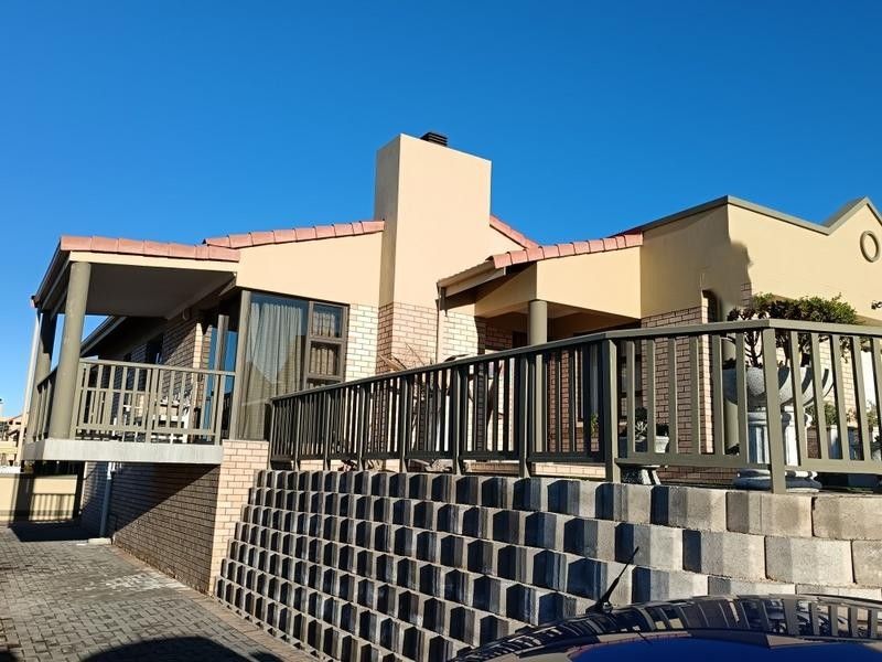 Rear elevation of the house featuring a raised balcony, brick retaining wall, and chimney stack under a clear blue sky.