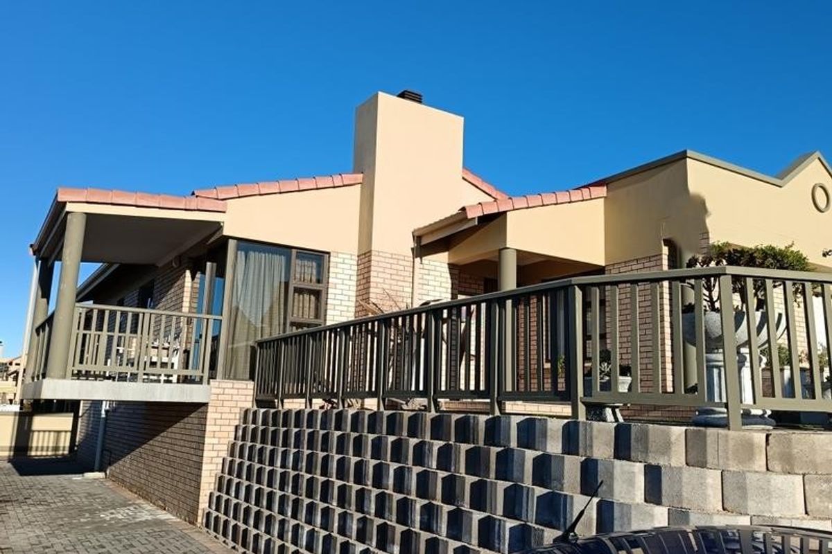 Rear elevation of the house featuring a raised balcony, brick retaining wall, and chimney stack under a clear blue sky.