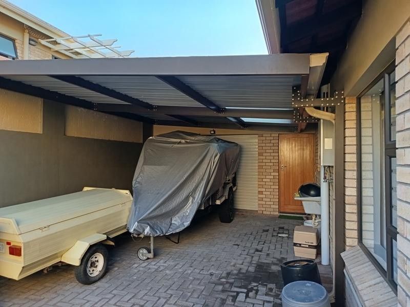 A covered carport area featuring brick paving, a wall-mounted gas geyser, and a utility sink, providing functional outdoor storage space.