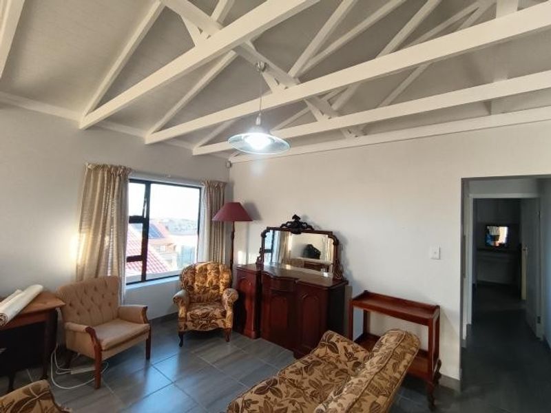 Living room featuring exposed white timber rafters, tiled flooring, and natural light through an aluminium-framed window.