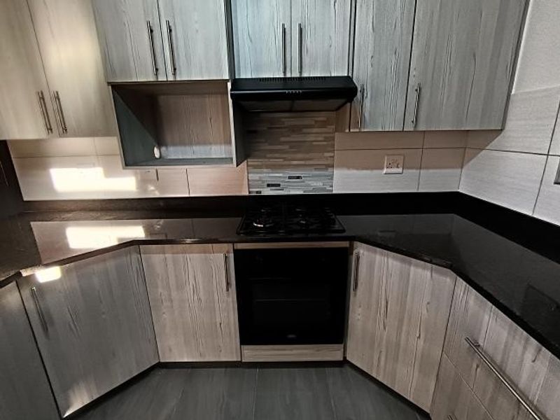 Modern kitchen featuring light wood-grain cabinetry, dark granite countertops, a built-in gas hob, oven, and extractor fan with a decorative tiled backsplash.
