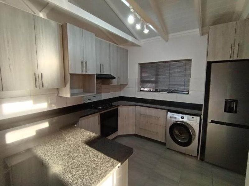 Modern kitchen featuring light wood-finish cabinetry, granite countertops, built-in oven, hob, and exposed beam ceilings with track lighting.