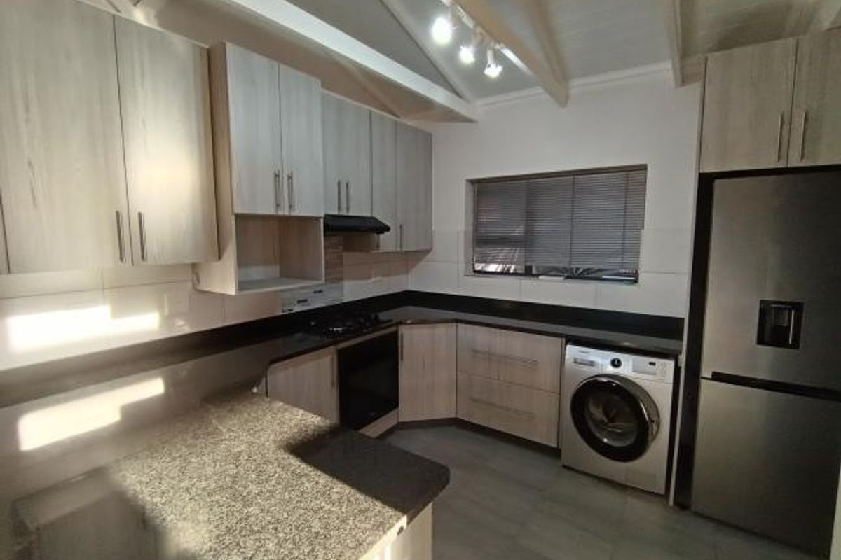 Modern kitchen featuring light wood-finish cabinetry, granite countertops, built-in oven, hob, and exposed beam ceilings with track lighting.