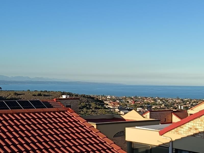 Elevated coastal view overlooking the surrounding residential neighbourhood and the ocean, featuring visible solar panels and tiled roofing.