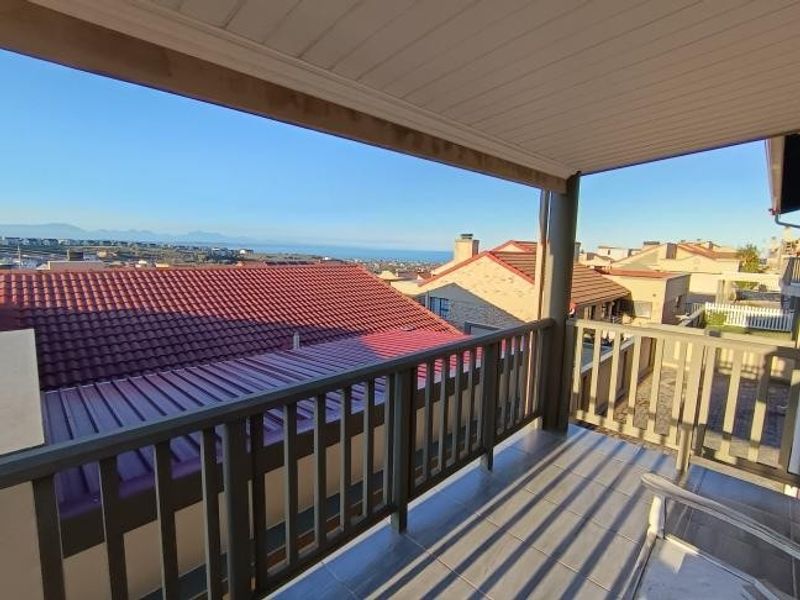 A covered balcony featuring tiled flooring and a railing, offering elevated views of the surrounding neighborhood and distant coastline.