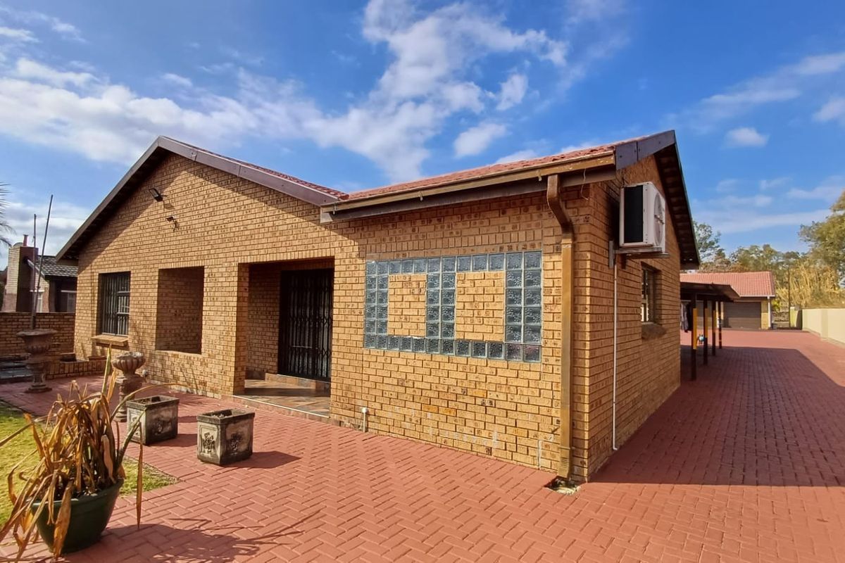 A well-maintained face brick exterior featuring a paved patio area, glass block window detailing, and an external air conditioning unit.
