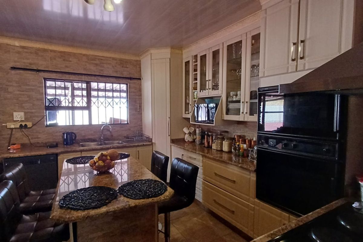 A functional kitchen featuring granite countertops, a central island, built-in cabinetry, and a double wall oven with an integrated extractor fan.