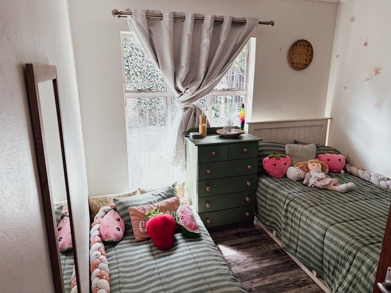 A cozy bedroom featuring laminate flooring and a window fitted with security bars, providing natural light and a view of the exterior.