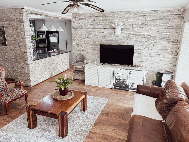 Open plan living area featuring a stone veneer feature wall, breakfast bar, and laminate flooring, seamlessly connecting to the kitchen space.
