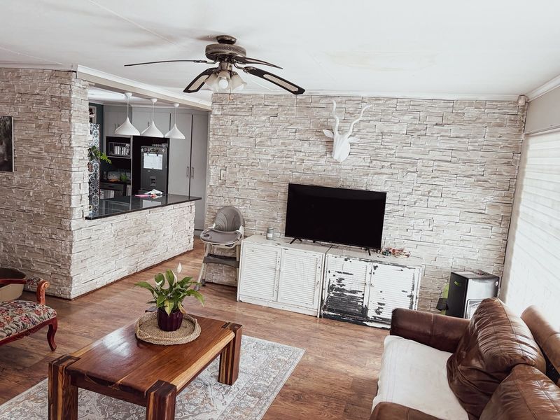 Open plan living area featuring a stone veneer accent wall, breakfast bar with granite countertop, and ceiling fan, connecting to the kitchen space.