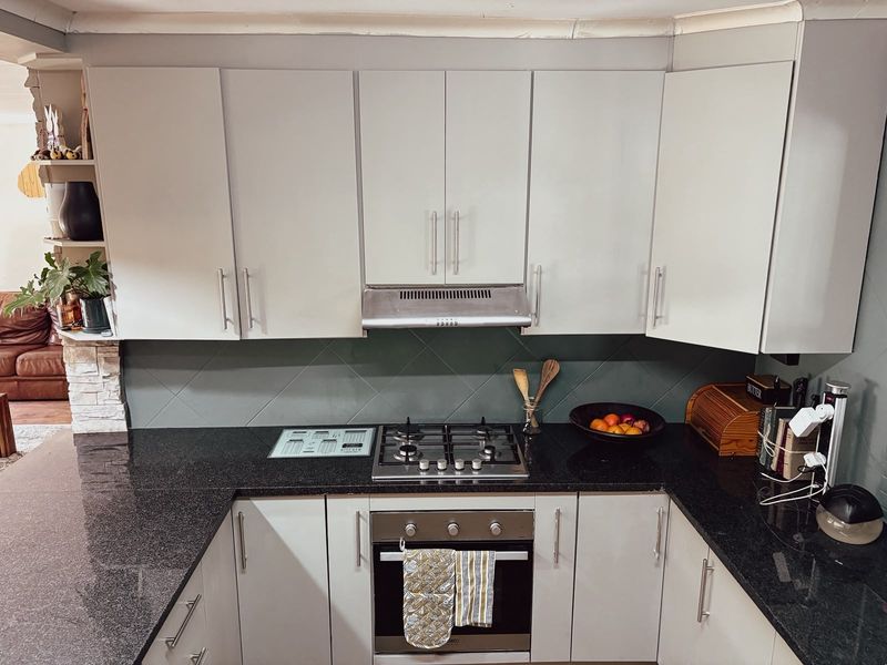A functional kitchen featuring granite countertops, a gas hob, built-in oven, extractor fan, and ample fitted cabinetry with a tiled backsplash.