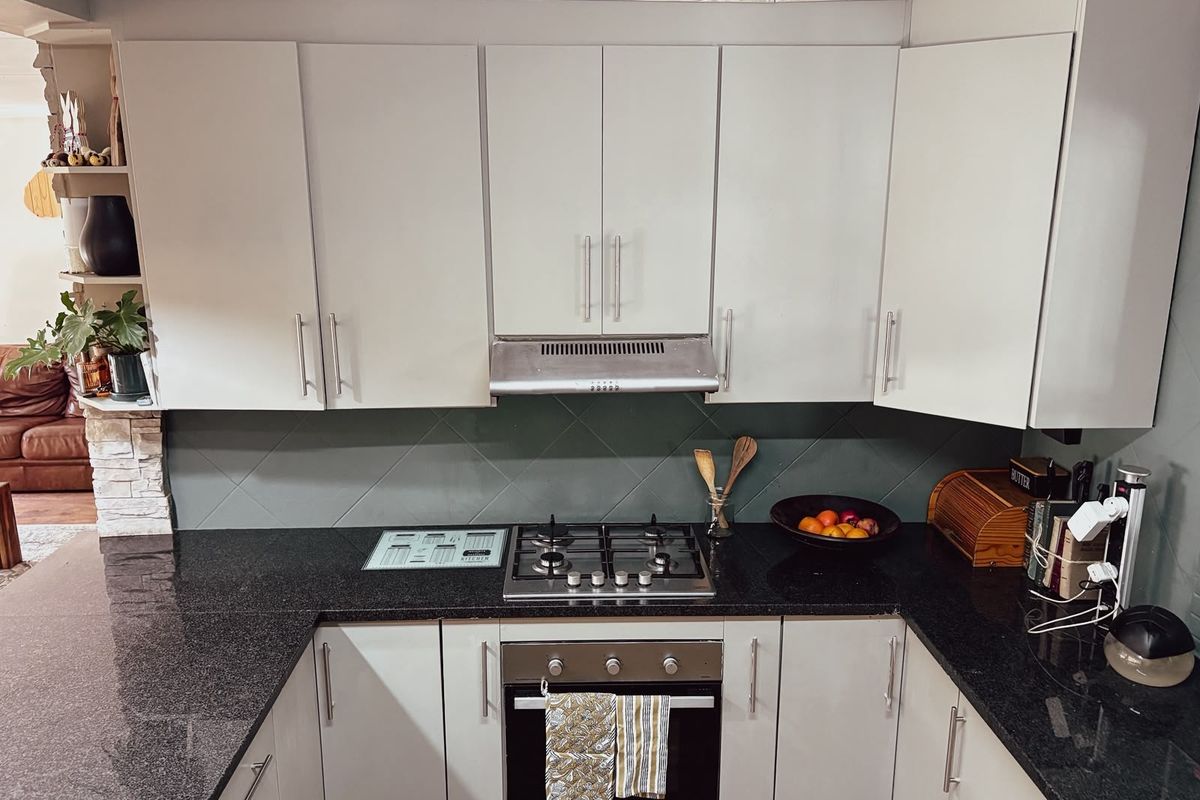A functional kitchen featuring granite countertops, a gas hob, built-in oven, extractor fan, and ample fitted cabinetry with a tiled backsplash.
