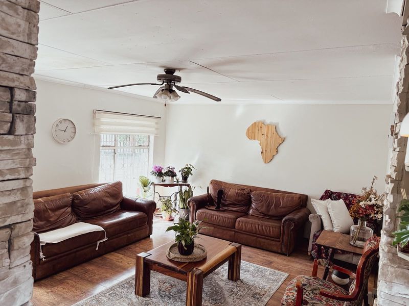 A comfortable living room featuring laminate flooring, a ceiling fan, and a distinctive brick feature wall, providing a warm and inviting atmosphere.