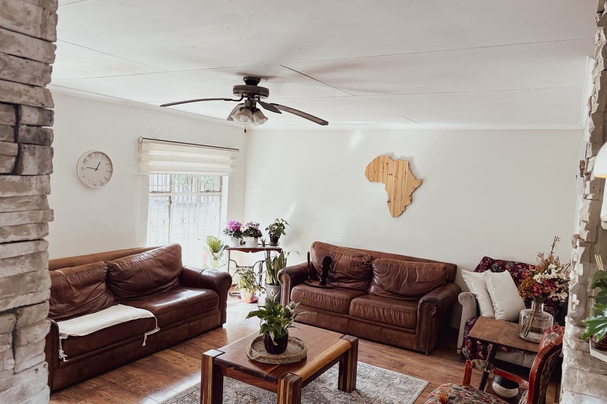 A comfortable living room featuring laminate flooring, a ceiling fan, and a distinctive brick feature wall, providing a warm and inviting atmosphere.