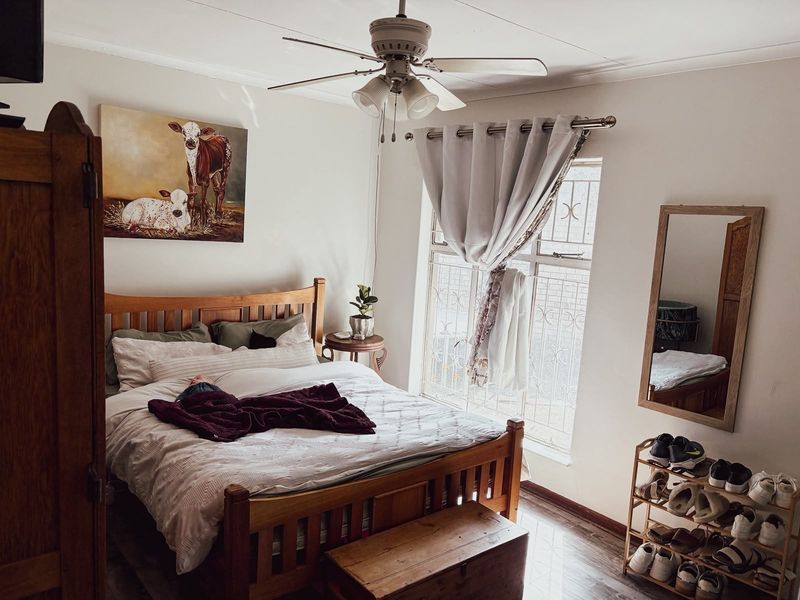 A cozy bedroom featuring a ceiling fan, laminate flooring, and a window fitted with a security gate.