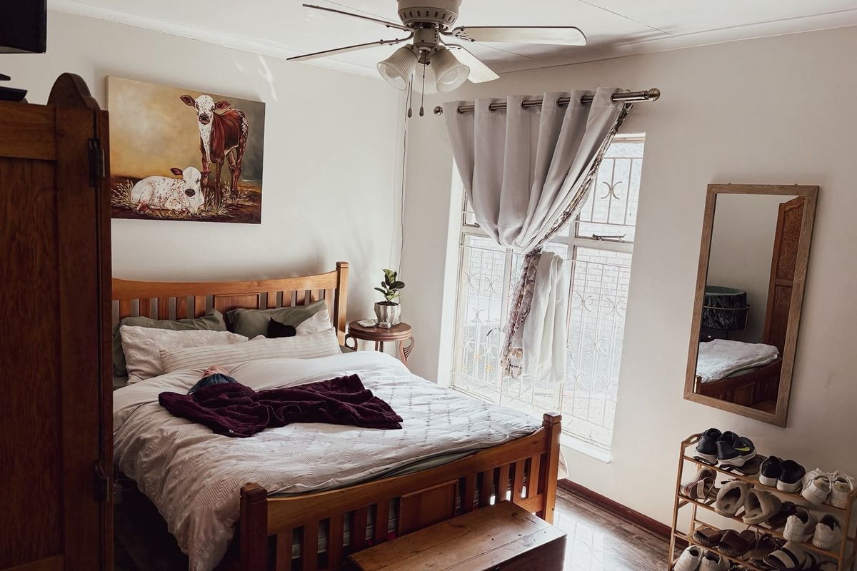 A cozy bedroom featuring a ceiling fan, laminate flooring, and a window fitted with a security gate.