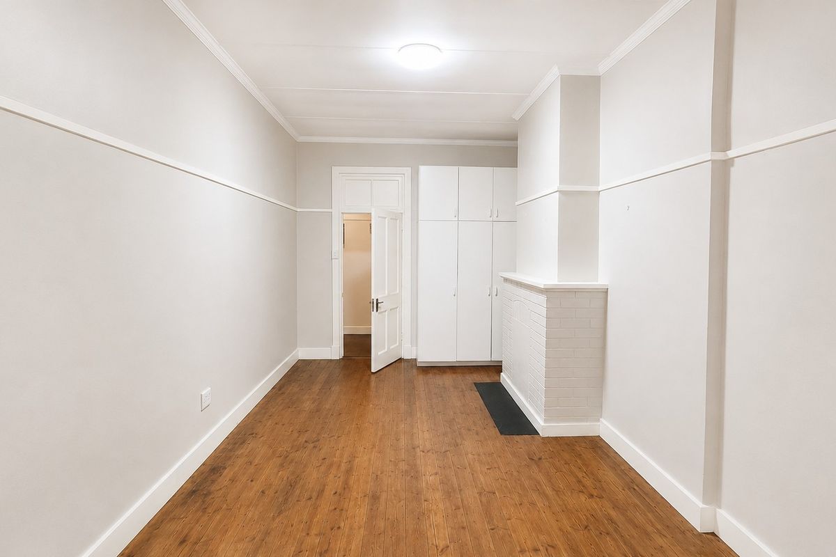 A bright, empty bedroom featuring polished timber flooring, built-in storage cupboards, and a classic fireplace surround with a picture rail.