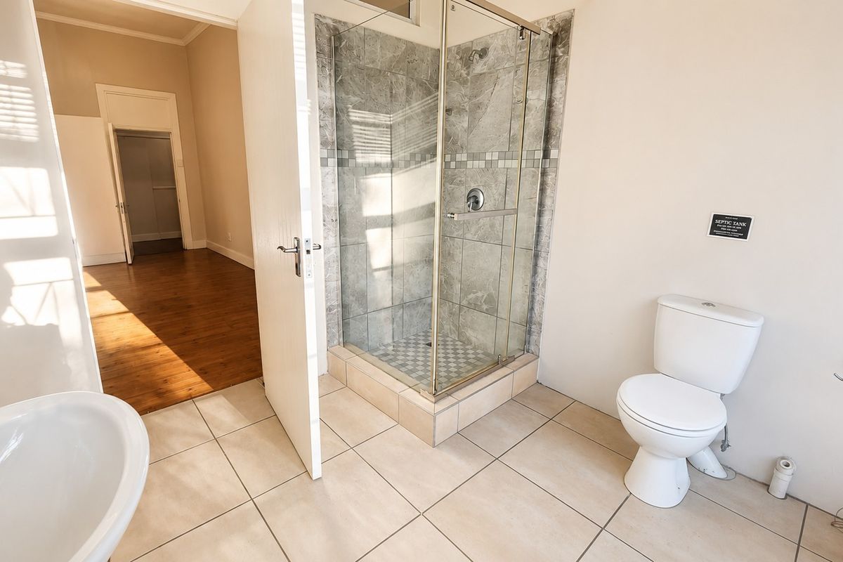 A clean, functional bathroom featuring a tiled shower enclosure, pedestal basin, and toilet, with neutral floor tiles and direct access to an adjacent room.