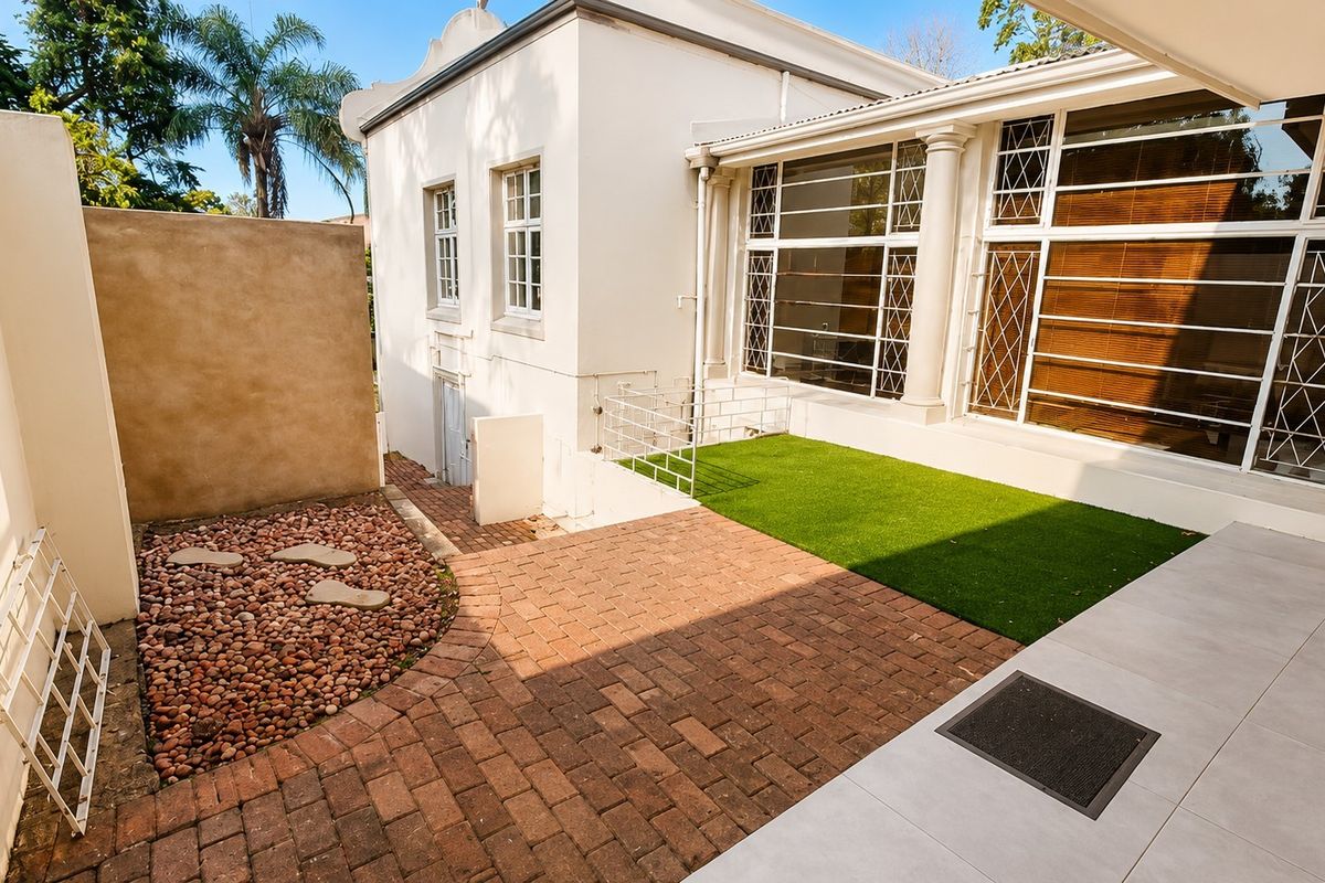 A well-maintained rear courtyard featuring brick paving, a small artificial grass area, and a pebble garden bed adjacent to the building's exterior.