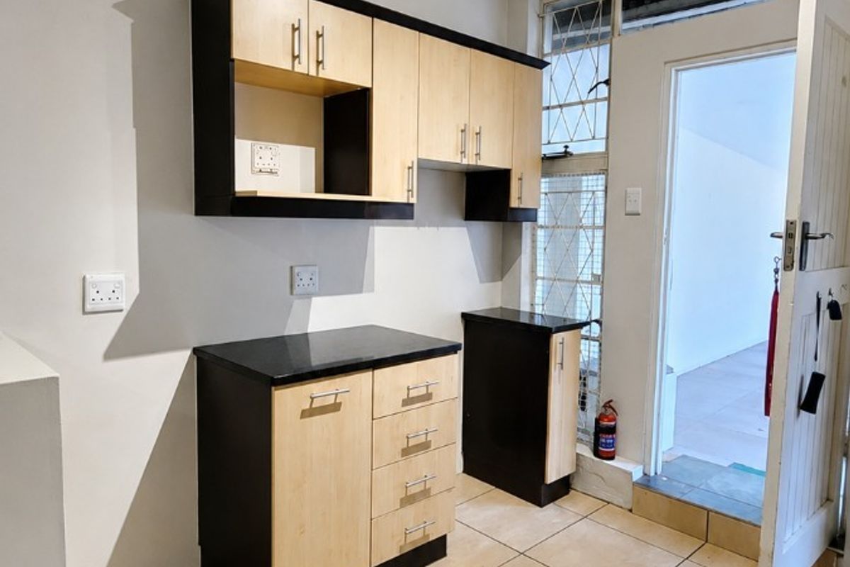 A compact kitchen area featuring built-in cabinetry with laminate countertops, ceramic tiled flooring, and direct access to an outdoor space via a security door.