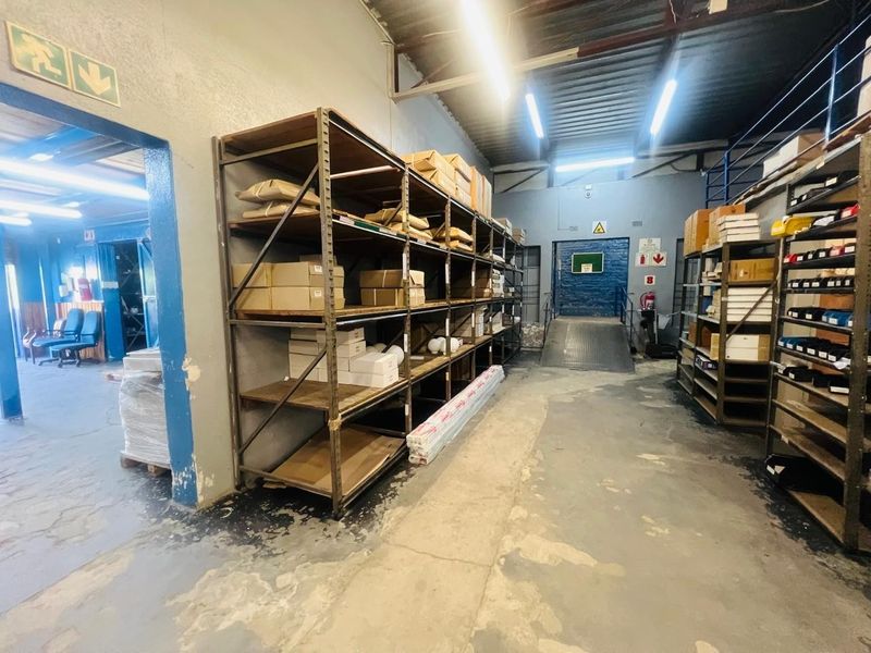 Industrial warehouse or storage area featuring concrete flooring, exposed steel roof structure, built-in metal shelving units, and a loading ramp for logistics access.