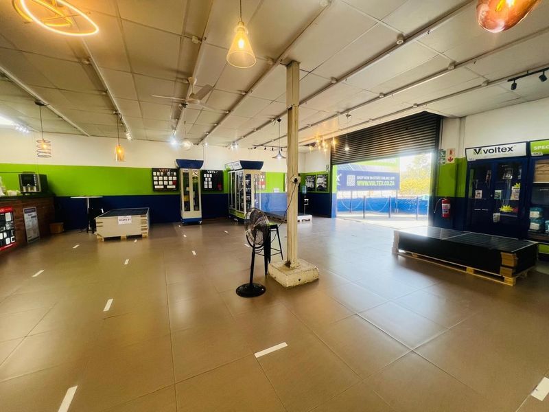 Spacious commercial open-plan showroom featuring tiled flooring, a high suspended ceiling, and a large roller shutter door for easy access.