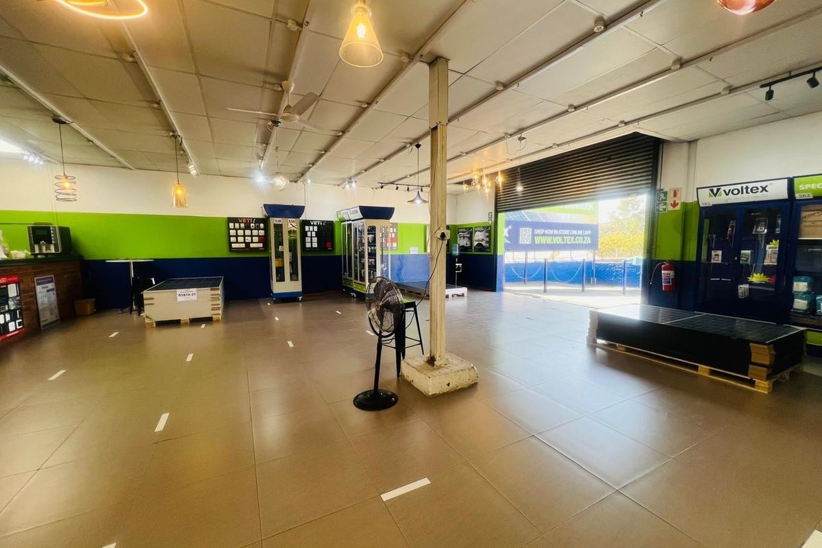 Spacious commercial open-plan showroom featuring tiled flooring, a high suspended ceiling, and a large roller shutter door for easy access.