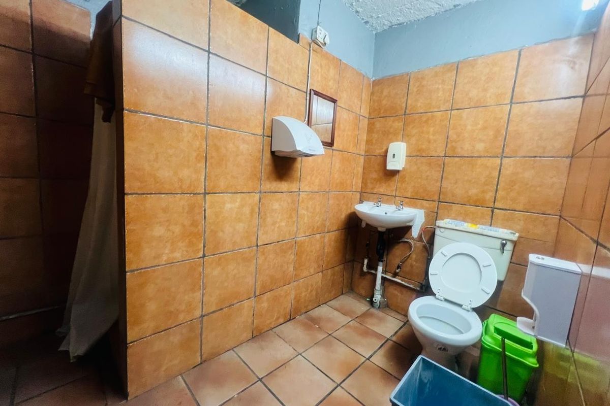 A functional commercial bathroom featuring full-height ceramic wall tiling, a pedestal basin, and standard sanitary fixtures.