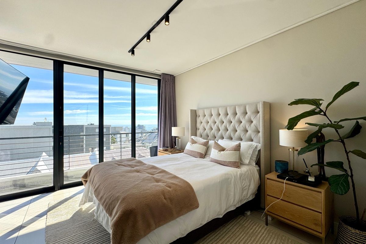 Modern bedroom featuring floor-to-ceiling sliding glass doors that provide ample natural light and access to a balcony with urban views.